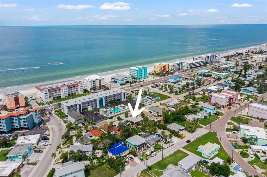 An aerial view shows a residential neighborhood near a beach with a white arrow pointing down — 14023 PALM STREET, MADEIRA BEACH, FL