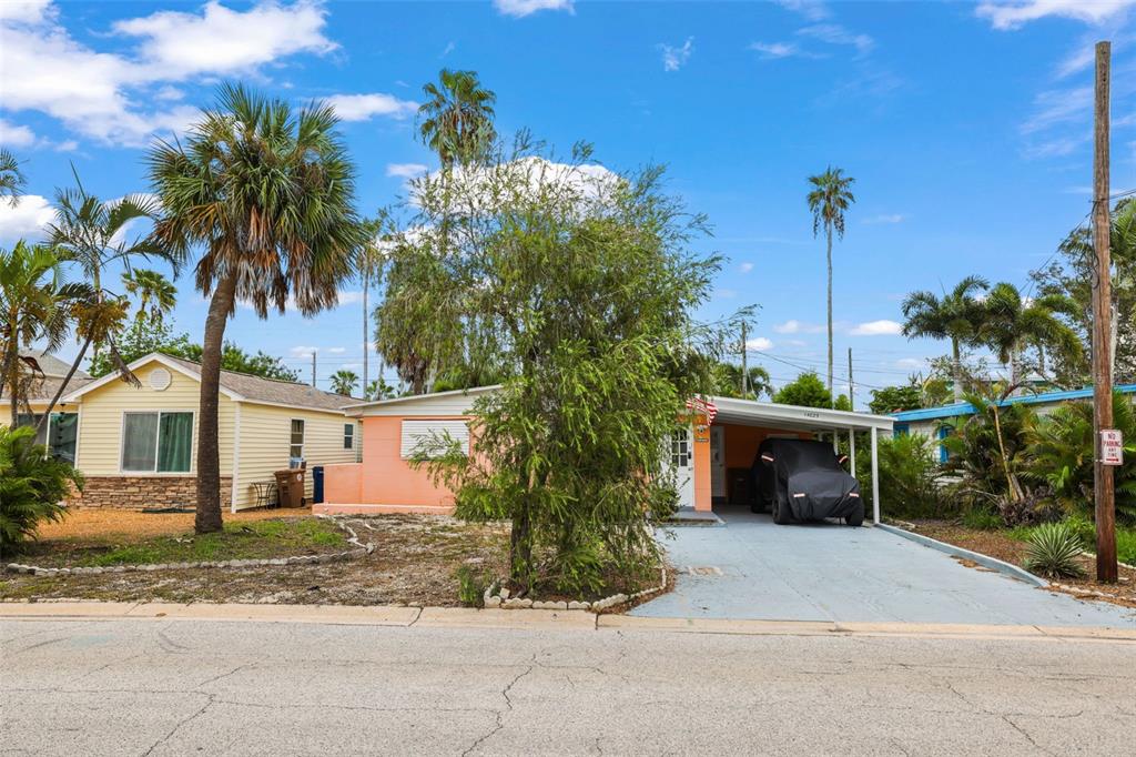 A peach-colored house with a carport and a palm tree stands along a paved street — 14023 PALM STREET, MADEIRA BEACH, FL