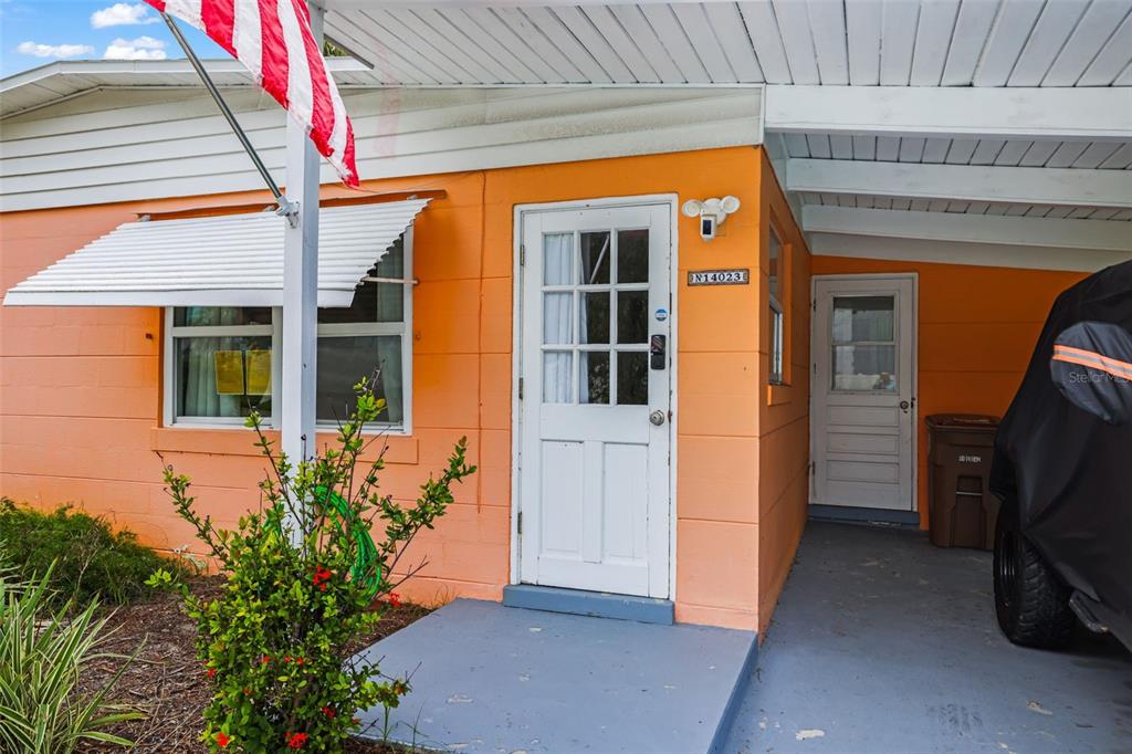 An orange exterior wall features a white front door, a window with an awning, and a carport — 14023 PALM STREET, MADEIRA BEACH, FL