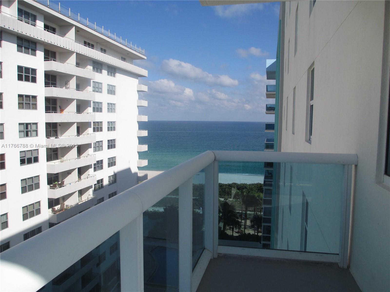 A balcony with a glass railing overlooks the ocean between two tall apartment buildings — 9201 Collins Ave # 1021, Surfside FL 33154, SURFSIDE, FL