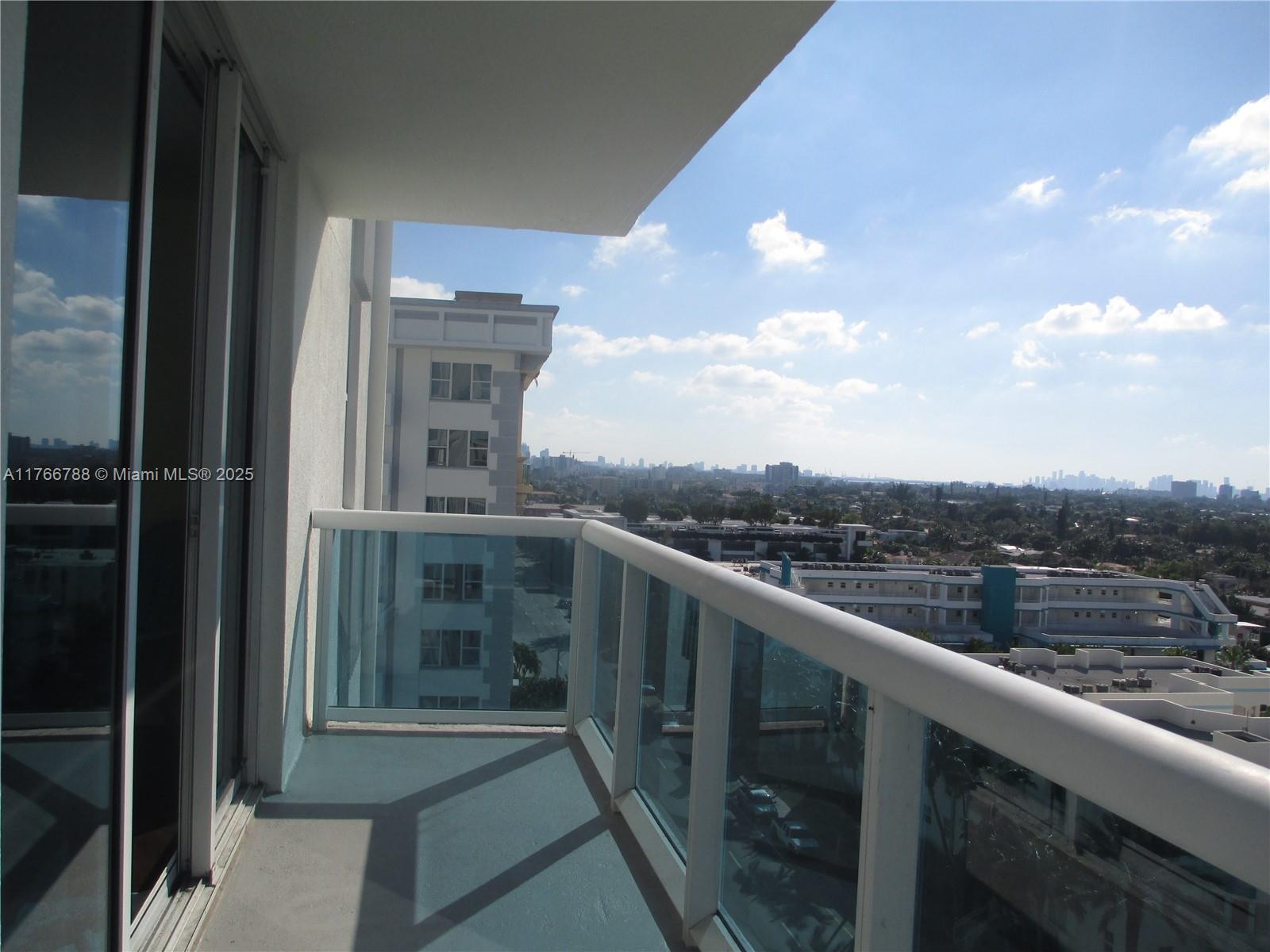 A balcony with a glass railing overlooks a city skyline under a blue sky — 9201 Collins Ave # 1021, Surfside FL 33154, SURFSIDE, FL