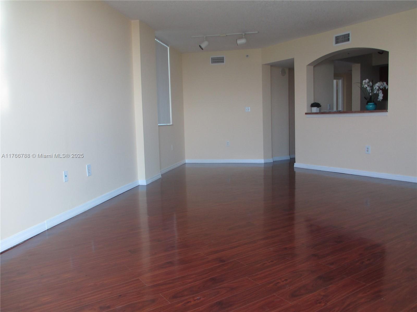 An empty room with dark wood flooring, light-colored walls, and a kitchen pass-through window — 9201 Collins Ave # 1021, Surfside FL 33154, SURFSIDE, FL