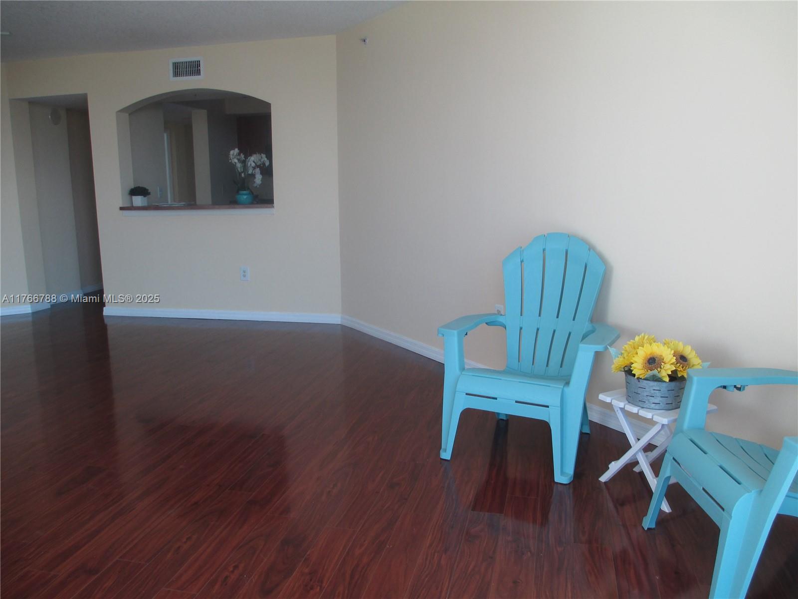 An empty room with dark wood floors, beige walls, and two light blue Adirondack chairs — 9201 Collins Ave # 1021, Surfside FL 33154, SURFSIDE, FL