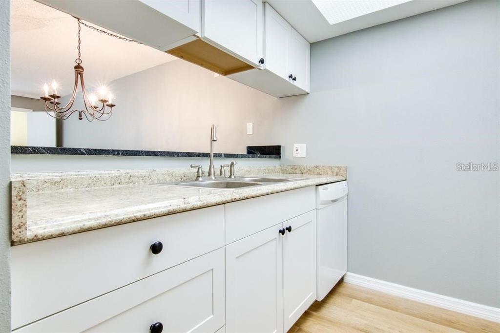 A kitchen features white cabinets, granite countertops, a stainless steel sink, and a dishwasher — 2615 COVE CAY DRIVE UNIT 205, CLEARWATER, FL
