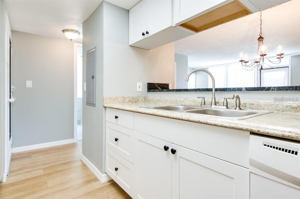 A kitchen features white cabinets, granite countertops, a stainless steel sink, and light wood flooring — 2615 COVE CAY DRIVE UNIT 205, CLEARWATER, FL