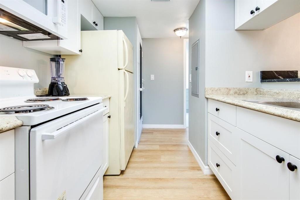 A kitchen features white cabinets, a light-colored refrigerator, a white stove, and wood-look flooring — 2615 COVE CAY DRIVE UNIT 205, CLEARWATER, FL