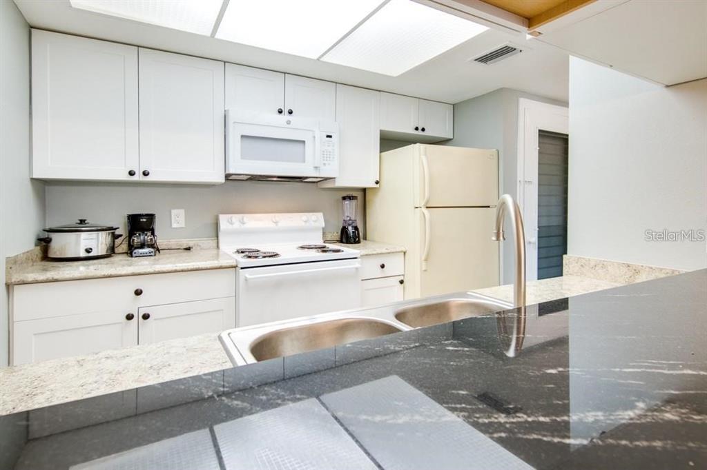 A kitchen features white cabinets, granite countertops, a black island counter, and a white refrigerator — 2615 COVE CAY DRIVE UNIT 205, CLEARWATER, FL