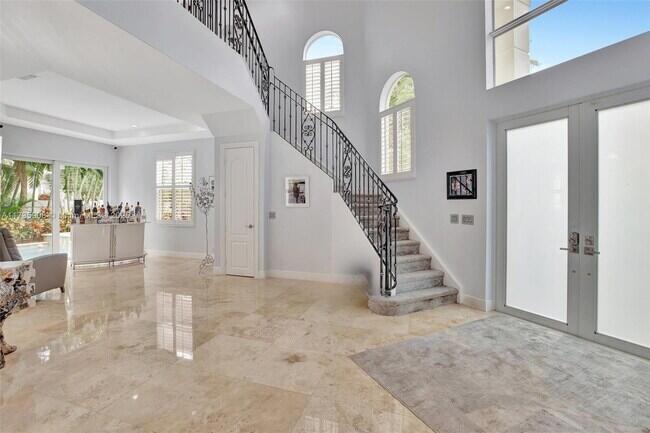 A bright foyer features a grand staircase with iron railings, marble floors, and double doors — 2844 NE 26th Avenue, Lighthouse Point FL 33064, LIGHTHOUSE POINT, FL