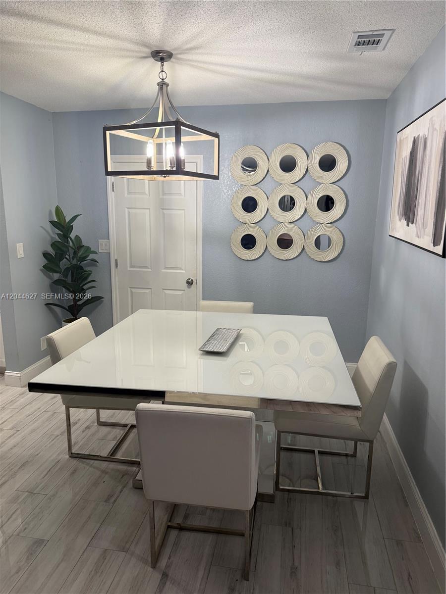 A dining room features a square white table, four chairs, and a modern light fixture — MARGATE, FL