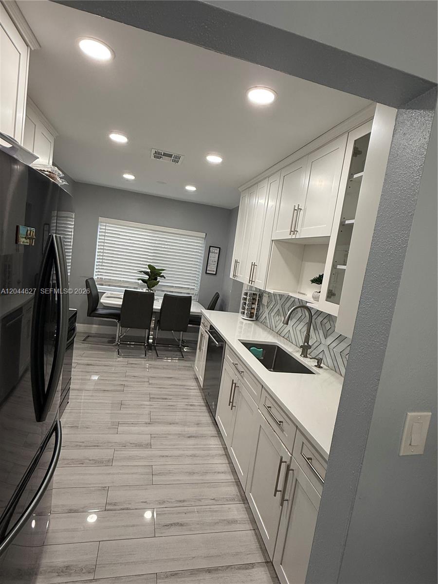 A modern kitchen features white cabinets, a patterned backsplash, and light wood-look tile flooring — MARGATE, FL