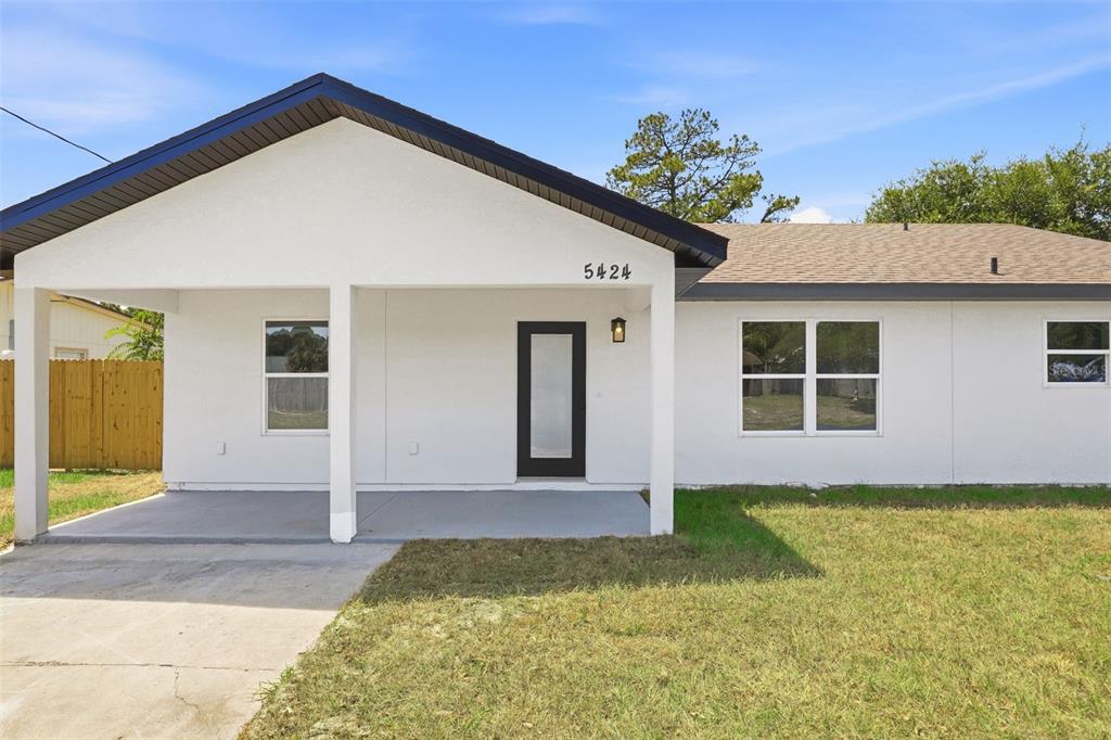 A white single-story house features a covered front porch, dark trim, and a modern door — 5424 FLINT ROAD, COCOA, FL