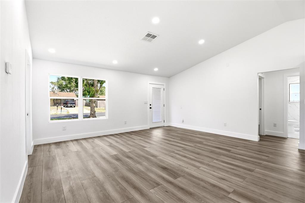 A bright, empty room features white walls, vaulted ceilings, and wood-look flooring — 5424 FLINT ROAD, COCOA, FL