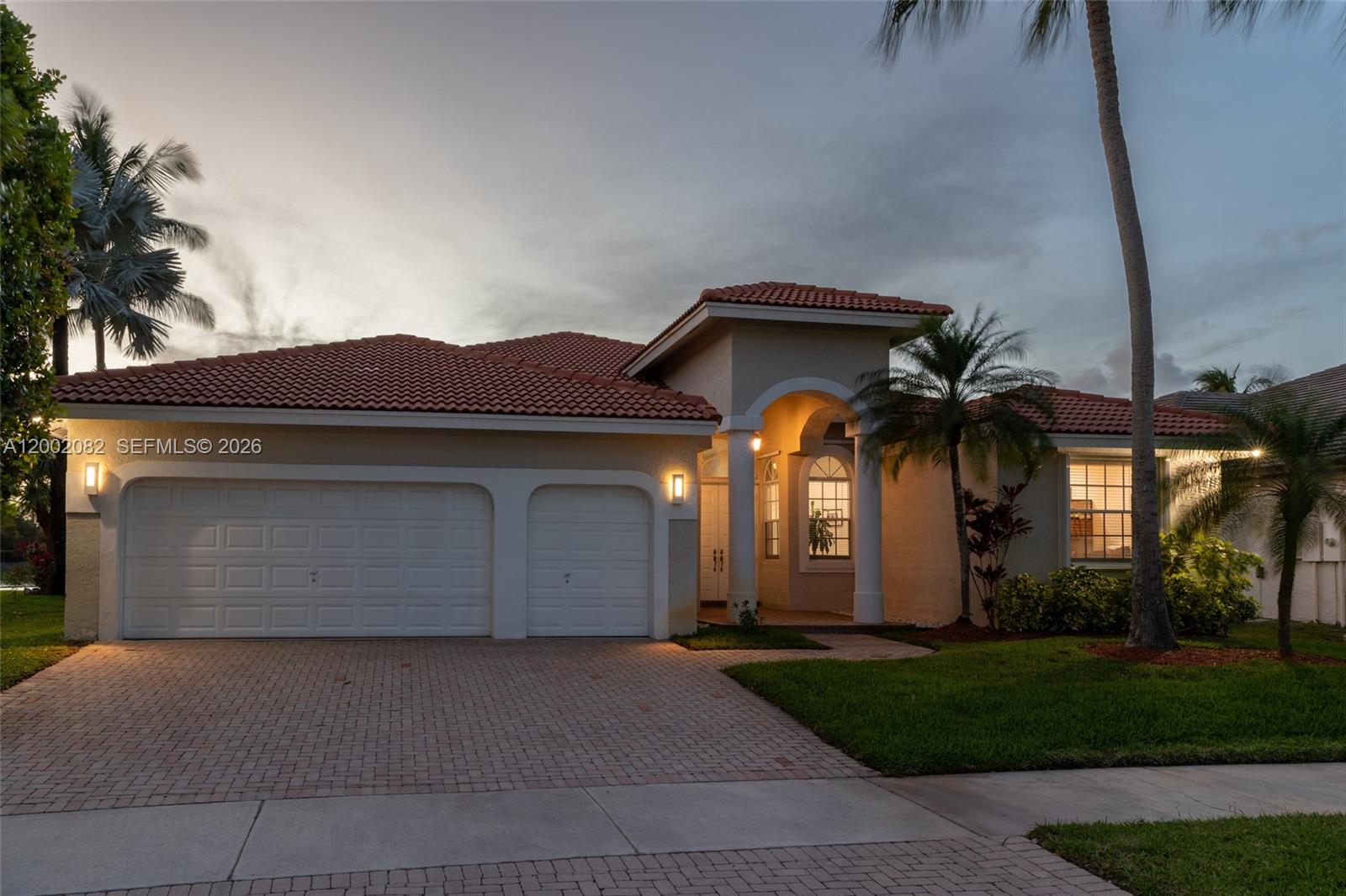 A single-story house with a tile roof, two-car garage, and palm trees at dusk — 2557 Jardin Ter, Weston FL 33327, WESTON, FL