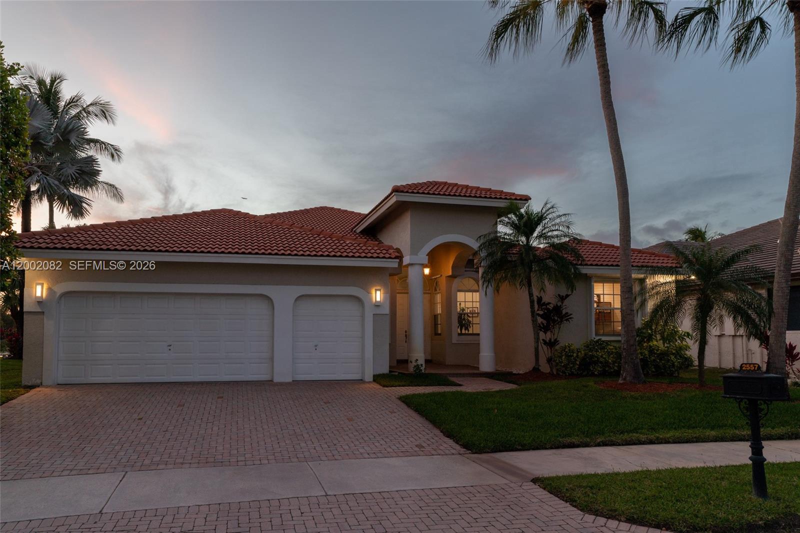 A single-story house with a tiled roof, two-car garage, and palm trees at dusk — 2557 Jardin Ter, Weston FL 33327, WESTON, FL