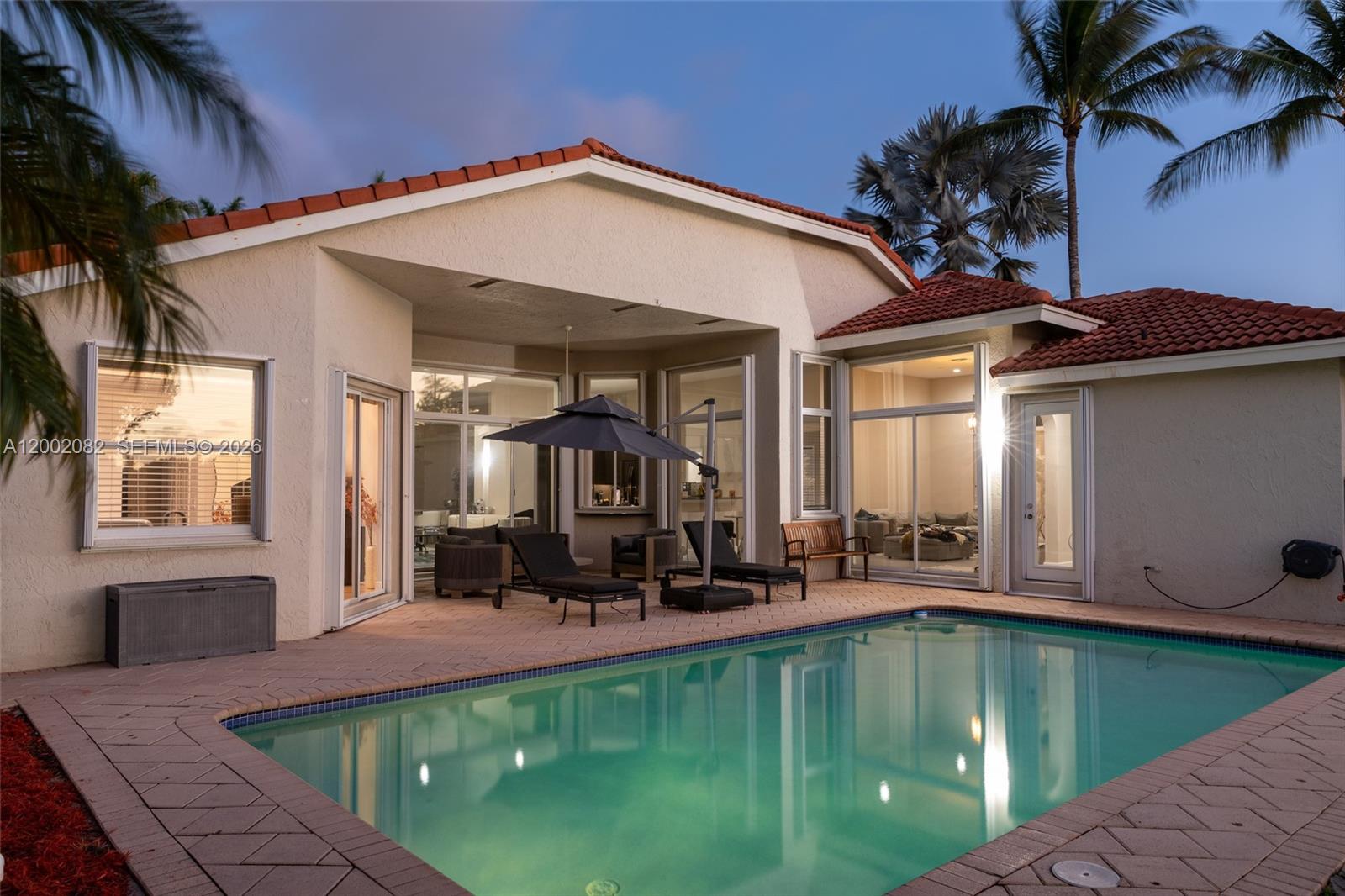 A backyard swimming pool sits in front of a house with a covered patio area — 2557 Jardin Ter, Weston FL 33327, WESTON, FL