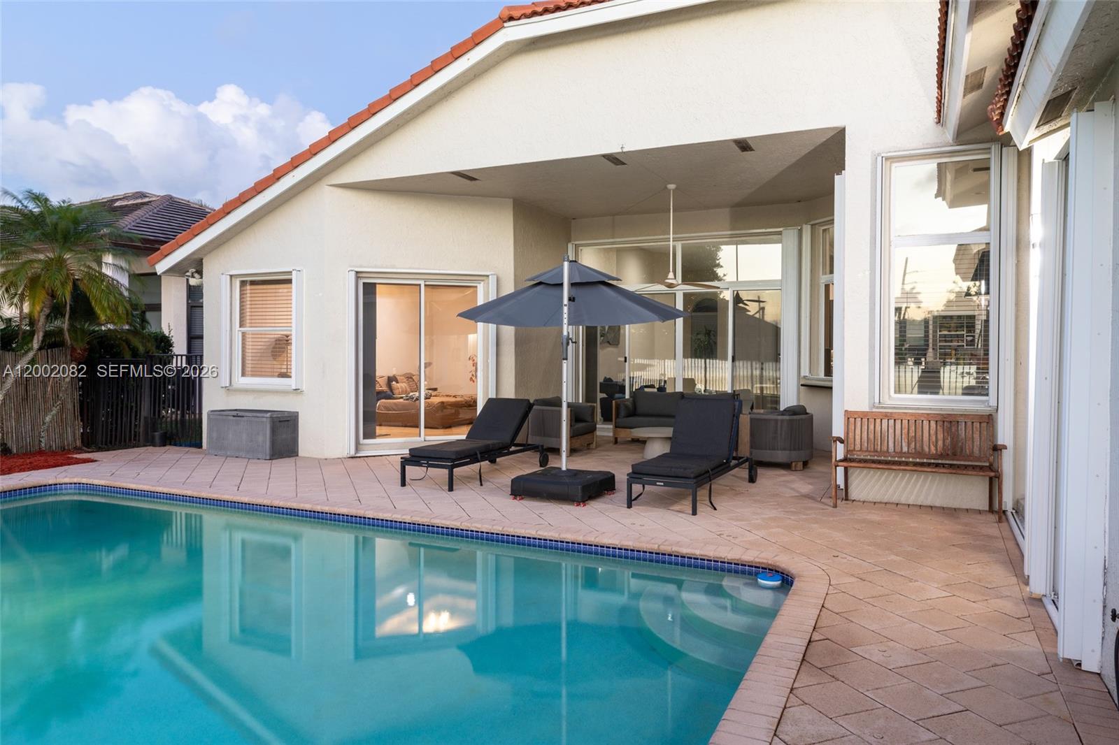 A patio with lounge chairs and an umbrella overlooks a swimming pool behind a house — 2557 Jardin Ter, Weston FL 33327, WESTON, FL