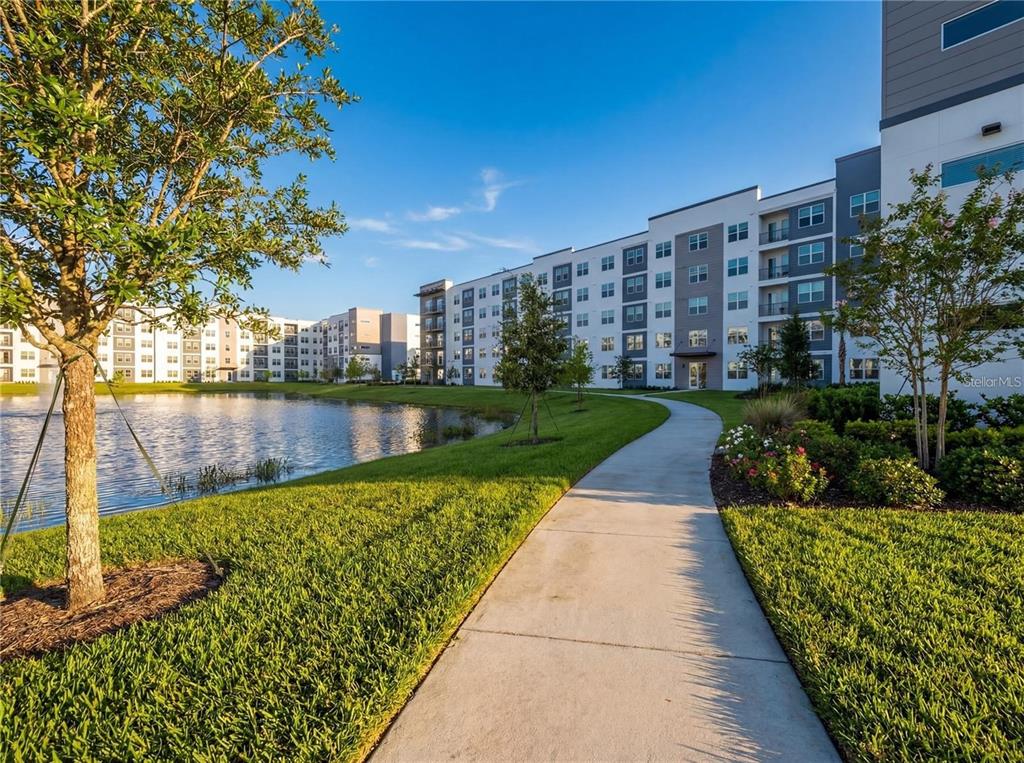 A concrete walkway leads past a pond toward a large, multi-story apartment building — 5579 MILLENIA BOULEVARD UNIT 515, ORLANDO, FL