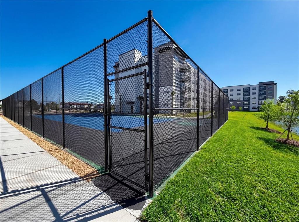 A fenced-in blue sports court sits next to a large apartment building and grassy lawn — 5579 MILLENIA BOULEVARD UNIT 515, ORLANDO, FL
