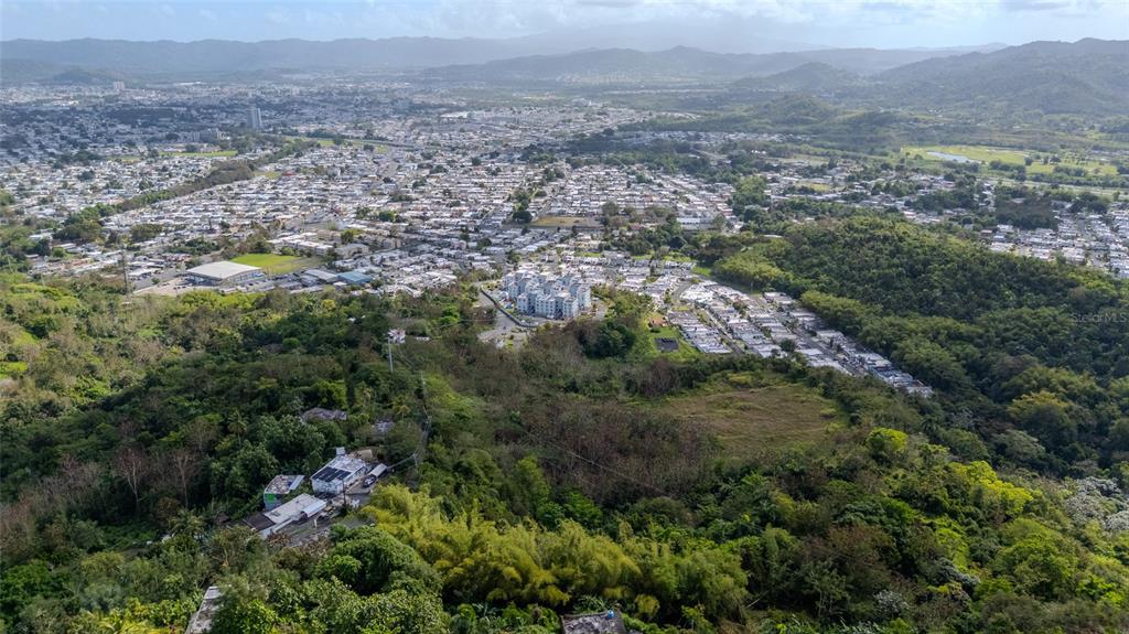 An aerial view shows a residential neighborhood nestled among hills and dense green vegetation — PR 7784 Km 1.0 TURABO, CAGUAS, PR