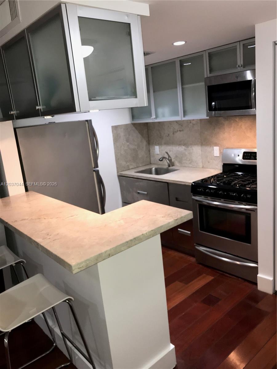 A small kitchen features stainless steel appliances, dark wood cabinets, and a light-colored breakfast bar — 731 6th St, Miami Beach FL 33139, MIAMI BEACH, FL