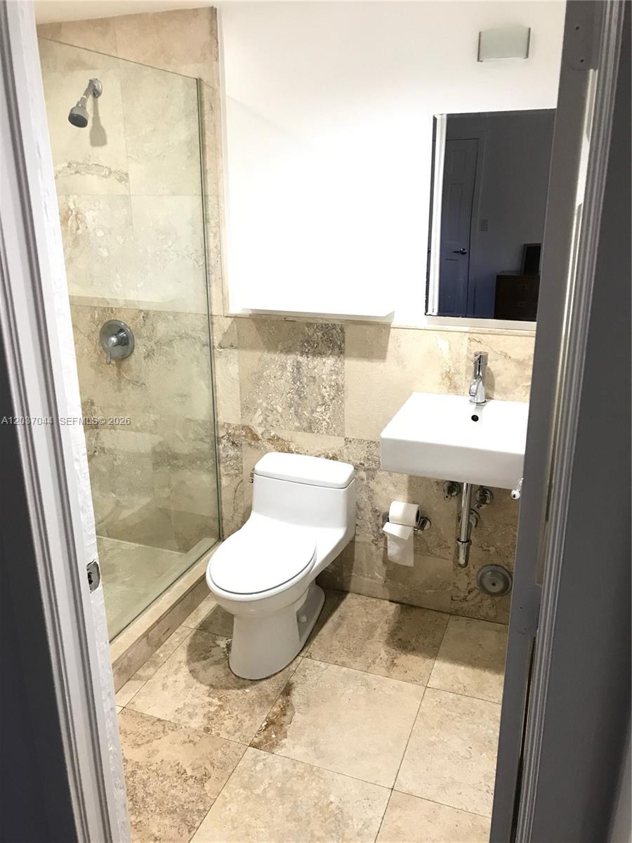 A small bathroom features a glass-enclosed shower, a wall-mounted sink, and beige stone tile — 731 6th St, Miami Beach FL 33139, MIAMI BEACH, FL