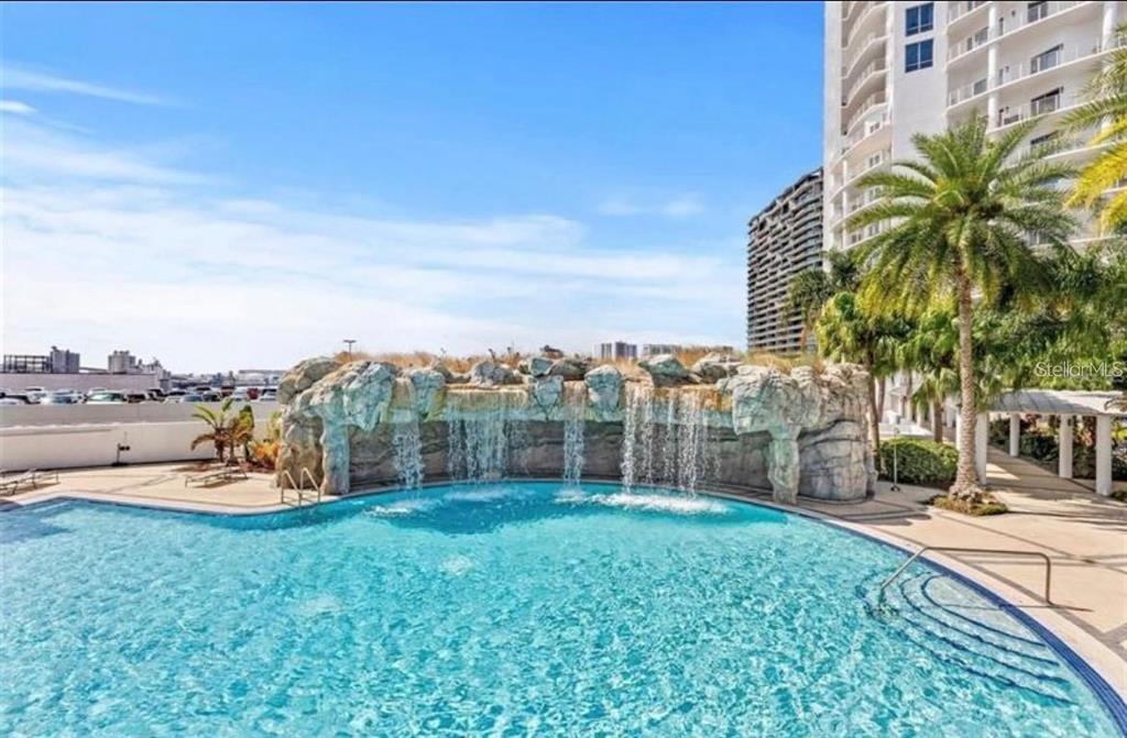A swimming pool features a large rock waterfall feature with a high-rise building in background — 1209 E CUMBERLAND AVENUE UNIT 508, TAMPA, FL