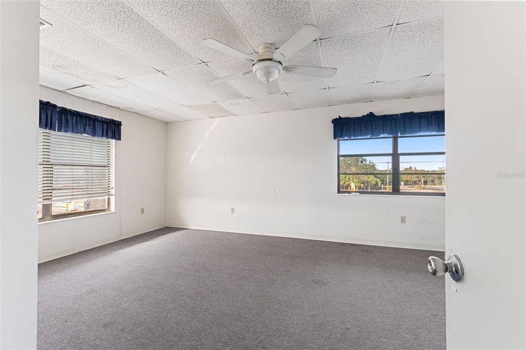 An empty room with gray carpeting, white walls, a drop ceiling, and two windows — 1108 COMMERCIAL WAY, SPRING HILL, FL