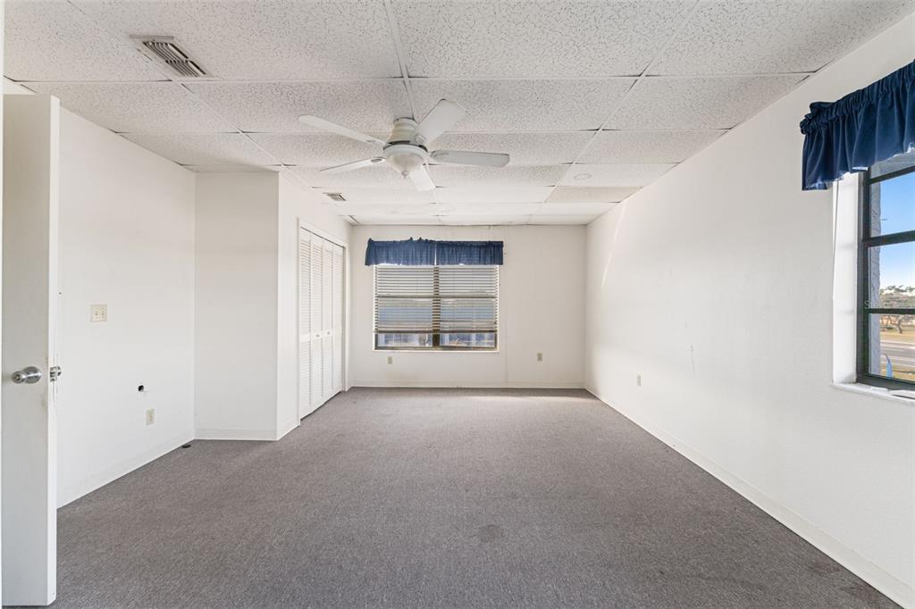 An empty room with gray carpeting, a drop ceiling, a ceiling fan, and two windows — 1108 COMMERCIAL WAY, SPRING HILL, FL