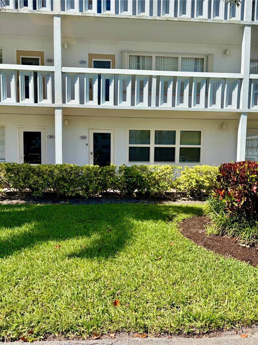The exterior of a two-story apartment building features white balconies, green landscaping, and numbered doors — 1044 Cambridge C, Deerfield Beach FL 33442, DEERFIELD BEACH, FL