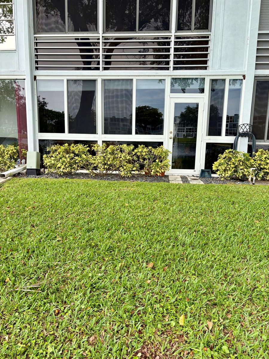The exterior of a ground-floor unit features large windows, a glass door, and landscaping — 1044 Cambridge C, Deerfield Beach FL 33442, DEERFIELD BEACH, FL