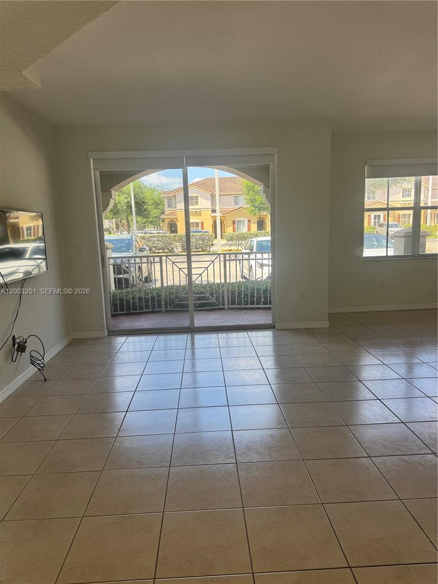 A living room features beige tile flooring, a sliding glass door, and a wall-mounted television — 8826 W Flagler St # 102, Miami FL 33174, MIAMI, FL