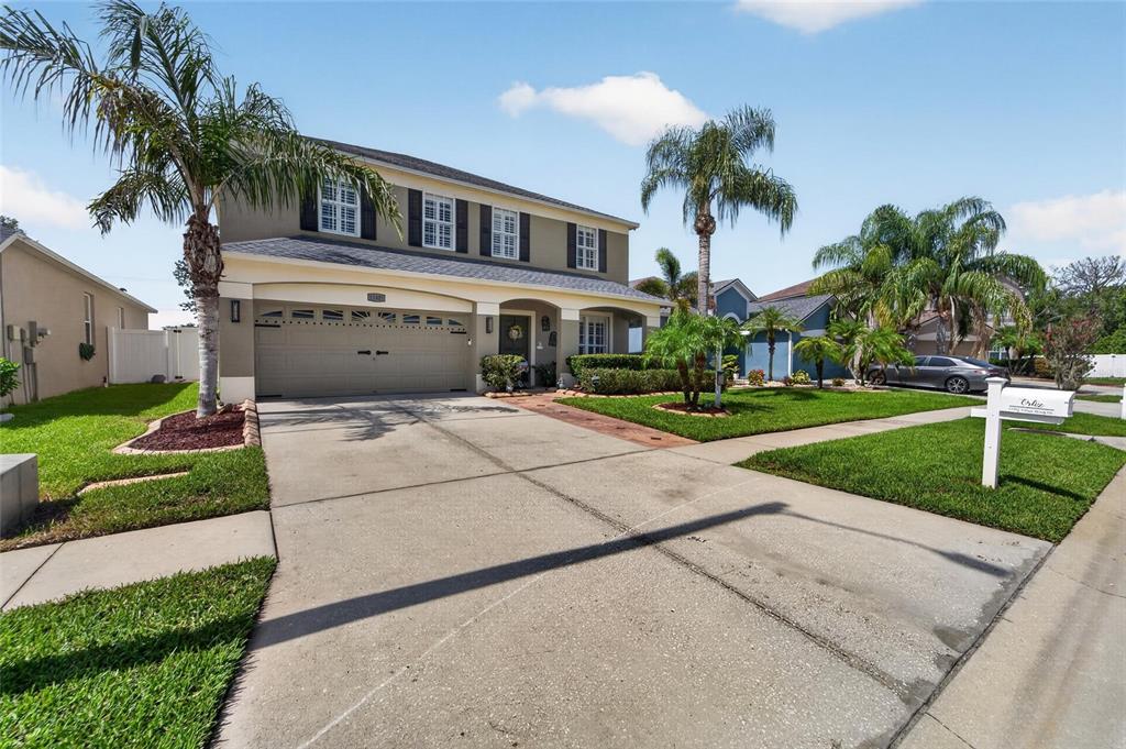 A two-story suburban house with a tan exterior, a two-car garage, and palm trees — 11405 VILLAGE BROOK DRIVE, RIVERVIEW, FL