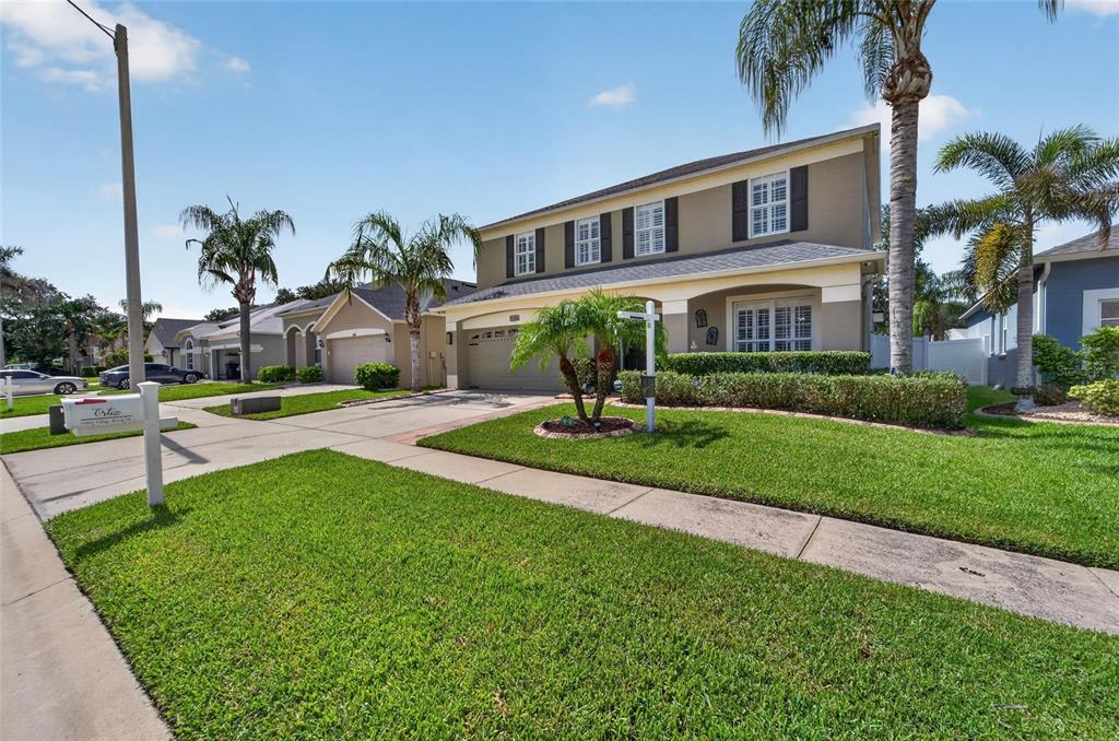A two-story suburban house with a tan exterior, dark shutters, and a manicured front lawn — 11405 VILLAGE BROOK DRIVE, RIVERVIEW, FL