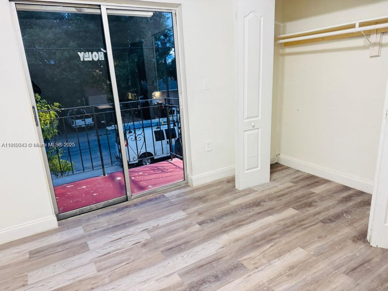 A room with wood-look flooring, a sliding glass door to a balcony, and an open closet — 932 NW 5th St, Miami FL 33128, MIAMI, FL