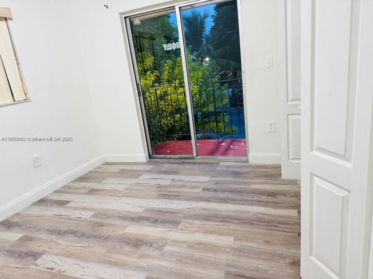 An empty room features wood-look flooring, white walls, and a sliding glass door to a balcony — 932 NW 5th St, Miami FL 33128, MIAMI, FL