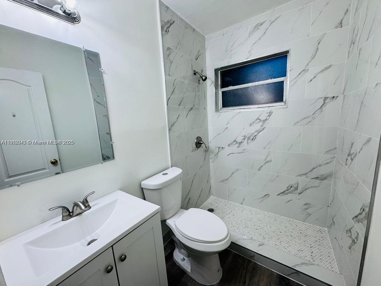 A bathroom features a white vanity, a toilet, and a walk-in shower with marble-look tiles — 932 NW 5th St, Miami FL 33128, MIAMI, FL