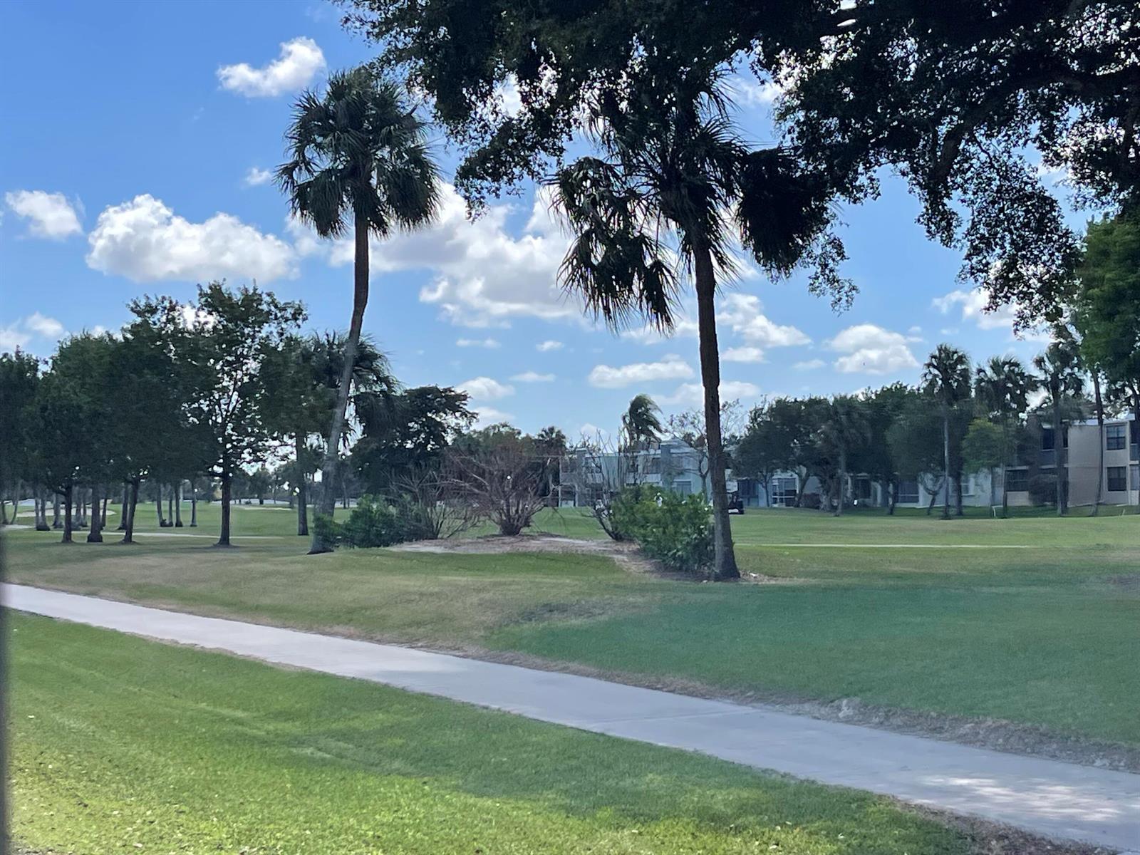 A paved path winds through a grassy golf course with palm trees and distant buildings — 7460 NW 18th Street # 104, Margate FL 33063, MARGATE, FL