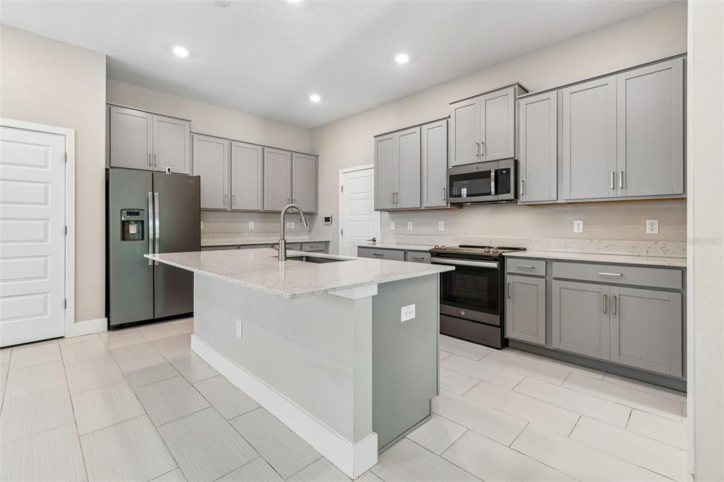 A kitchen features gray cabinetry, white countertops, a central island, and stainless steel appliances — 7409 S KISSIMMEE STREET, TAMPA, FL