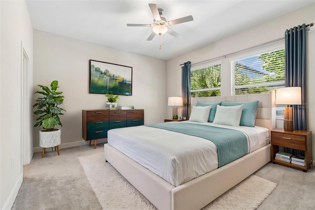A bedroom features a bed with teal bedding, a wooden dresser, and a ceiling fan — 7409 S KISSIMMEE STREET, TAMPA, FL