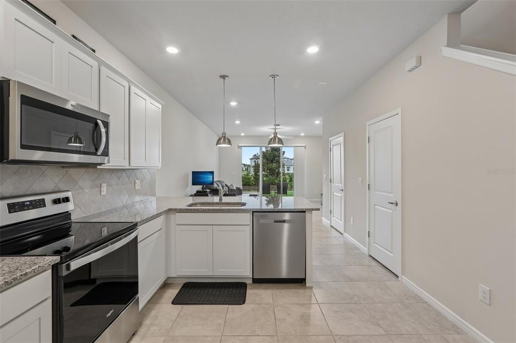 A kitchen with white cabinets, stainless steel appliances, and granite countertops overlooks a living area — 31337 AMBERVIEW BEND, WESLEY CHAPEL, FL
