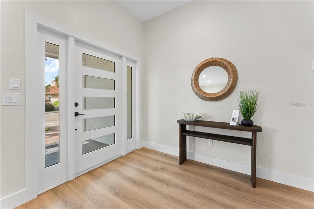 An entryway features a modern white front door, light wood flooring, and a console table — 4973 60TH AVENUE S, ST PETERSBURG, FL