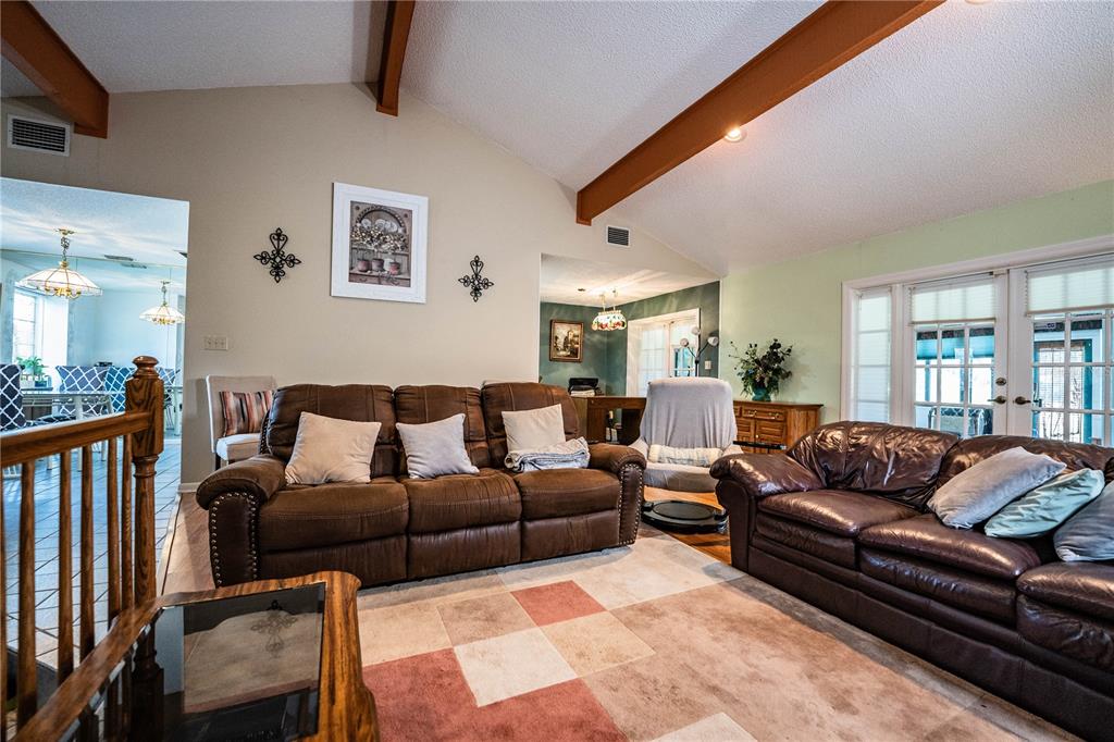 A living room features brown leather sofas, vaulted ceilings with exposed beams, and tile flooring — 85 COUNTRY CLUB LANE, MULBERRY, FL