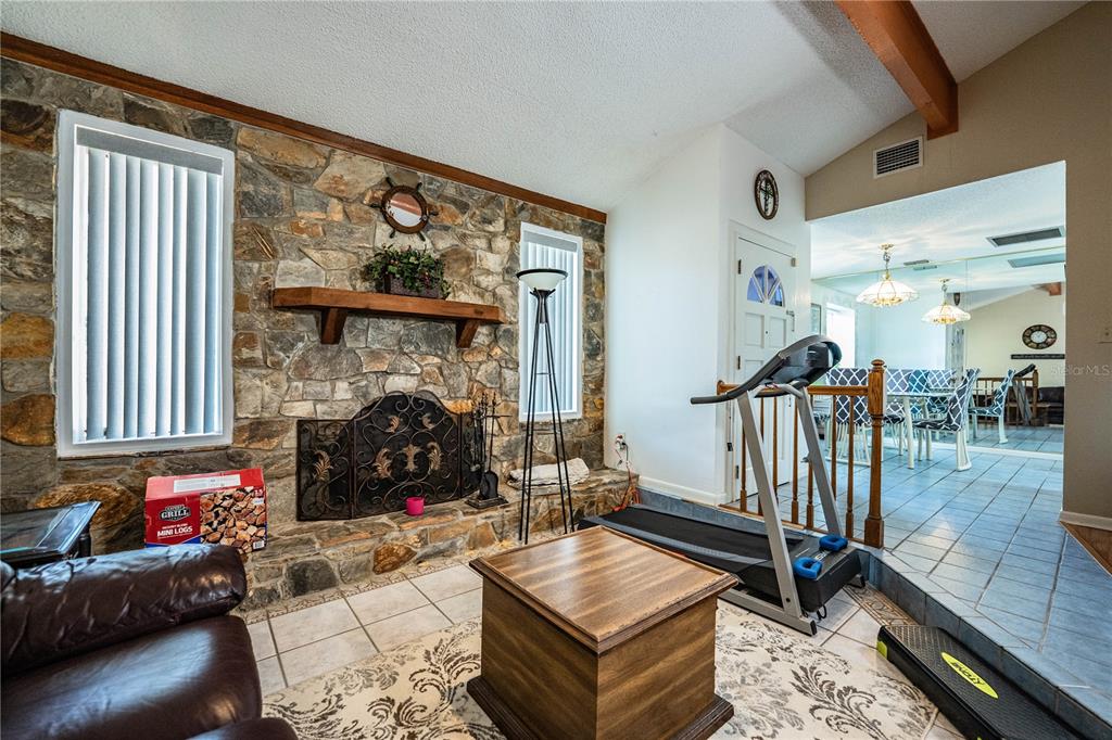 A living room features a stone fireplace, a treadmill, and tile flooring — 85 COUNTRY CLUB LANE, MULBERRY, FL