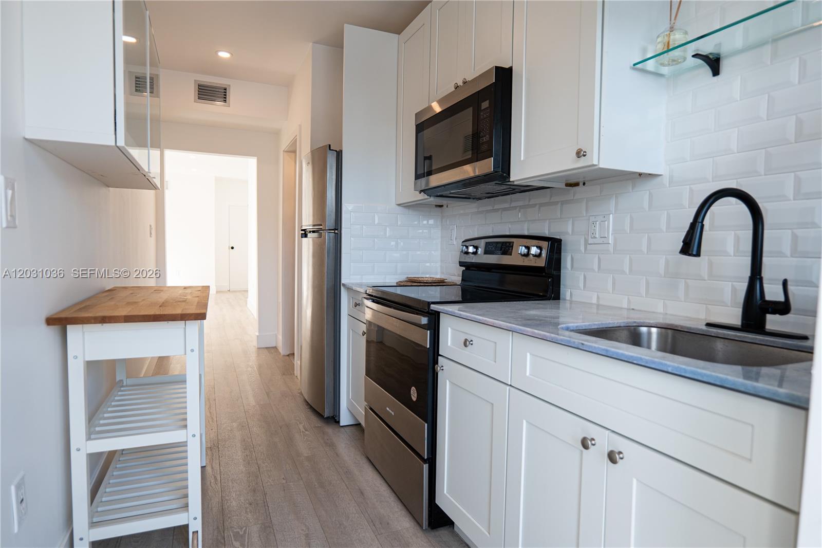 A galley kitchen features white cabinets, stainless steel appliances, a subway tile backsplash, and wood-look flooring — 1721 SW 13th St # 4, Miami FL 33145, MIAMI, FL