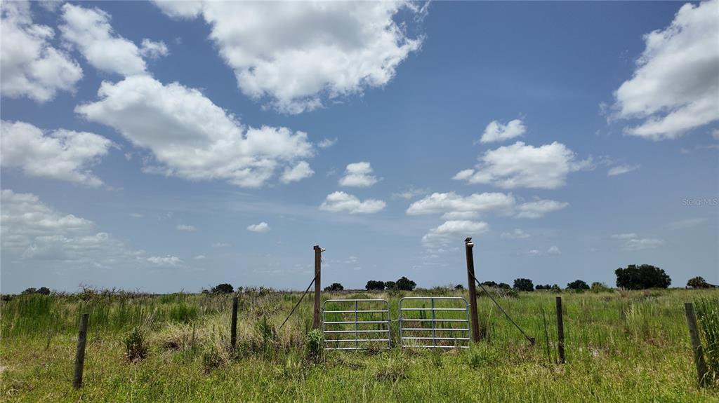 A metal gate stands in a grassy field under a bright, cloudy blue sky — 2001/2011 GRAHAM ROAD, PUNTA GORDA, FL