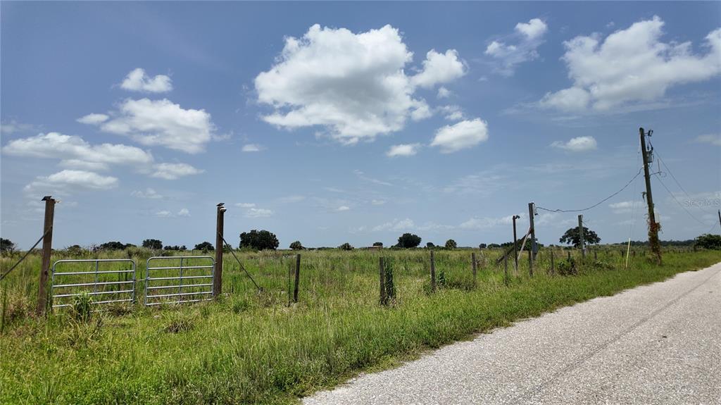 A gravel road runs alongside a fenced, grassy vacant lot under a blue sky — 2001/2011 GRAHAM ROAD, PUNTA GORDA, FL