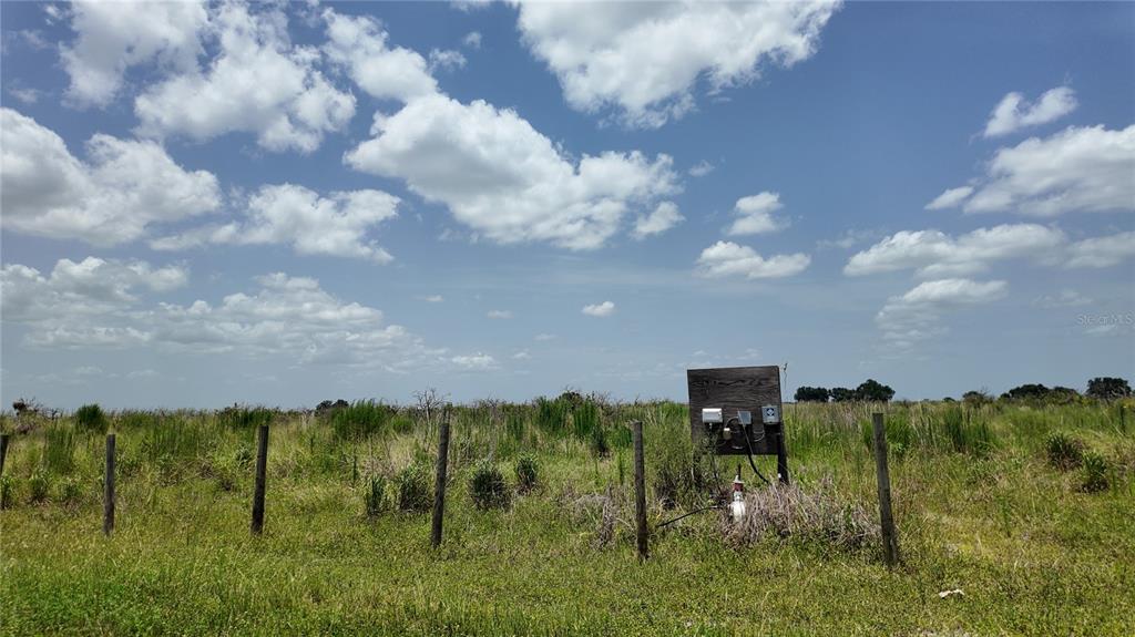 A wooden utility panel stands in a grassy field enclosed by a wire fence — 2001/2011 GRAHAM ROAD, PUNTA GORDA, FL
