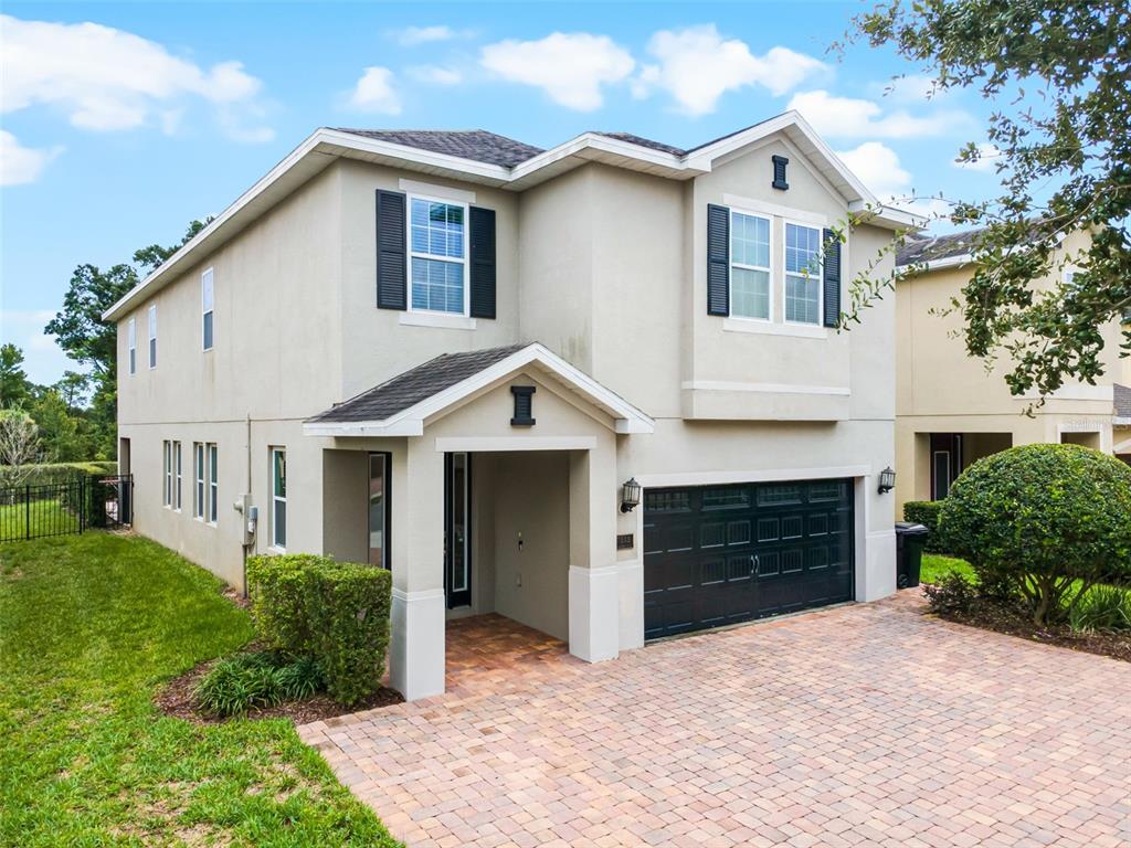 A two-story house with a beige stucco exterior, black garage door, and a brick paver driveway — 7513 MARKER AVENUE, KISSIMMEE, FL