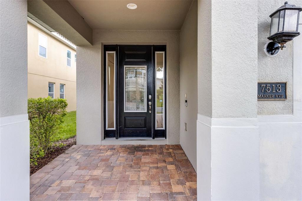 A covered entryway features a black front door with glass panels and stone paver flooring — 7513 MARKER AVENUE, KISSIMMEE, FL