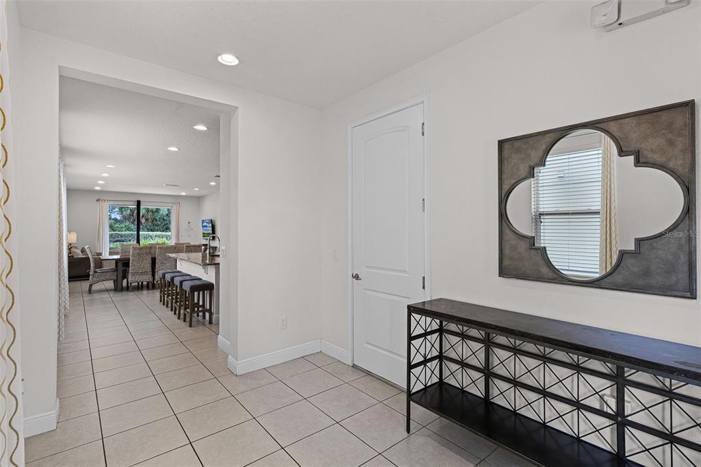 A tiled entryway features a console table, a decorative mirror, and a view into a kitchen — 7513 MARKER AVENUE, KISSIMMEE, FL